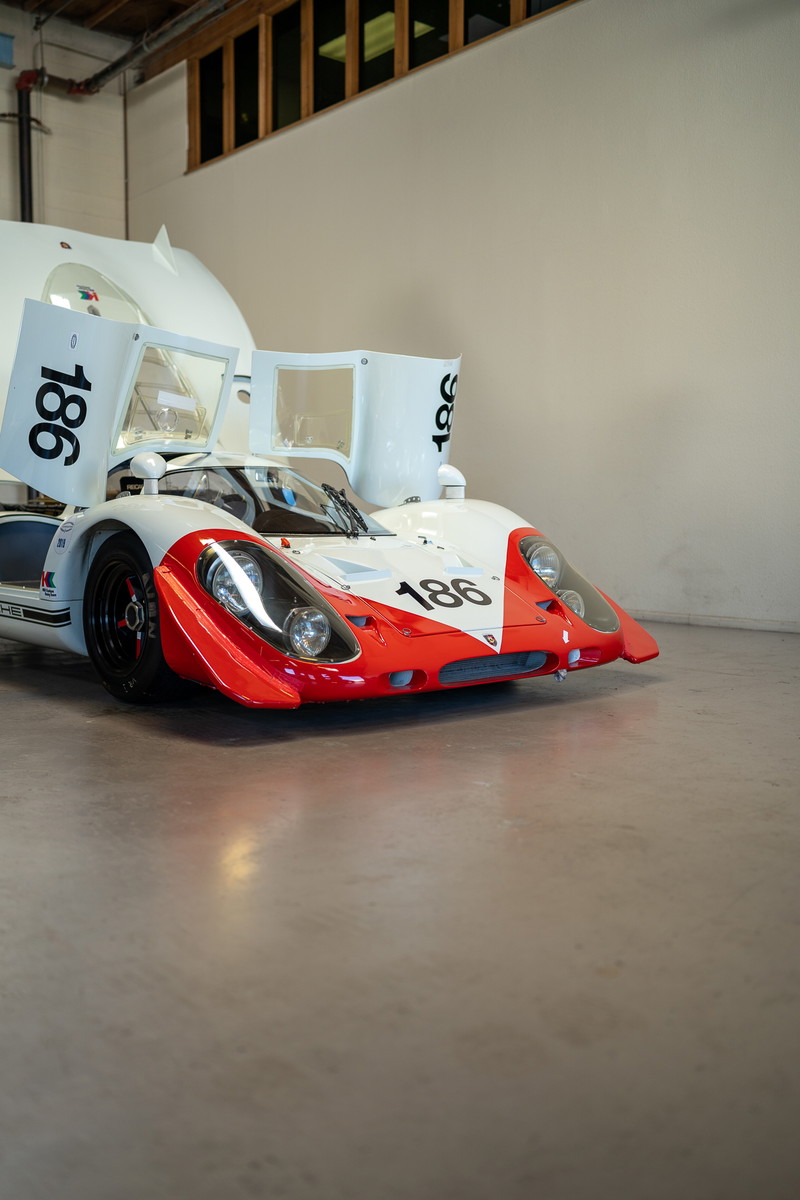 White Porsche 917 race car with red trim, number 186 livery, and gullwing doors open.