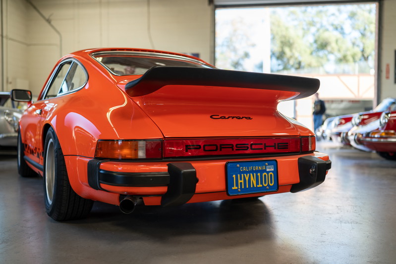 Orange 1970s Porsche 911 Carrera Targa with a black whale tail spoiler and black trim.