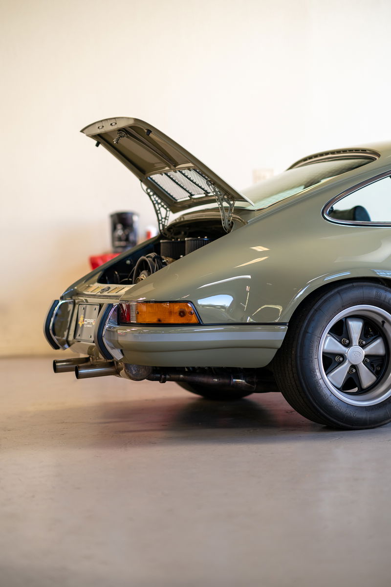 Porsche 911 Targa engine bay open, showing off the flat-six engine. Olive green paint with chrome trim.
