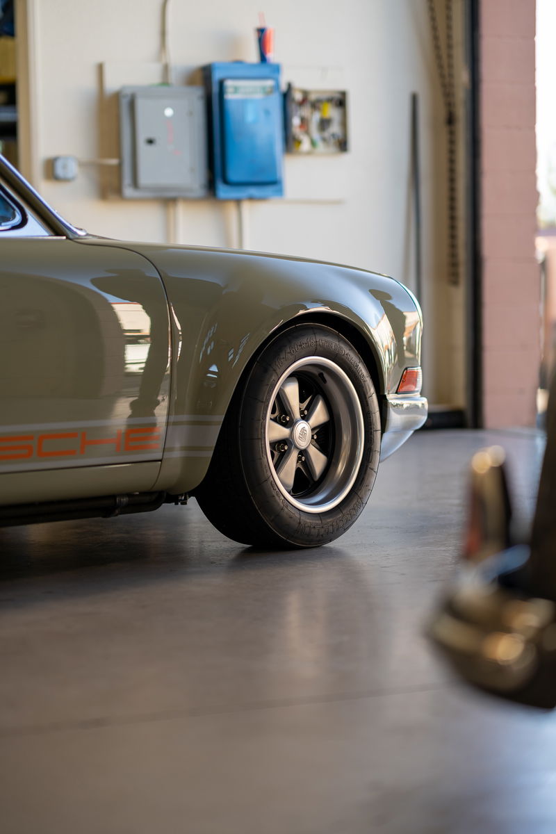 Close-up of a vintage Porsche 911 in olive green with orange livery, showing its Fuchs wheels.