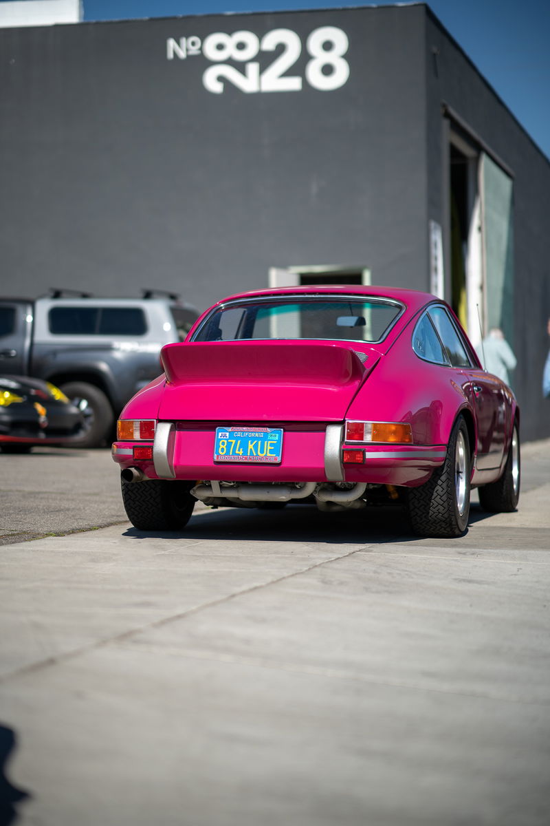 Rear view of a bright pink Porsche 911 with silver trim and Fuchs rims.