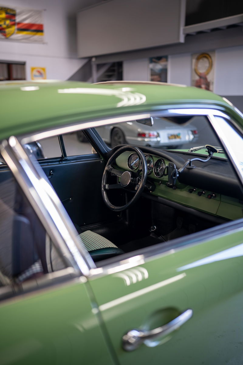 1960s Porsche 356 interior and green exterior. The car has a classic steering wheel and gauge cluster.