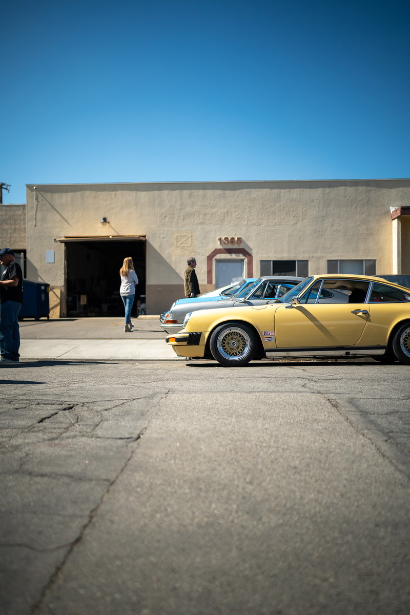 Yellow Porsche 911 with gold mesh rims parked outside a building.