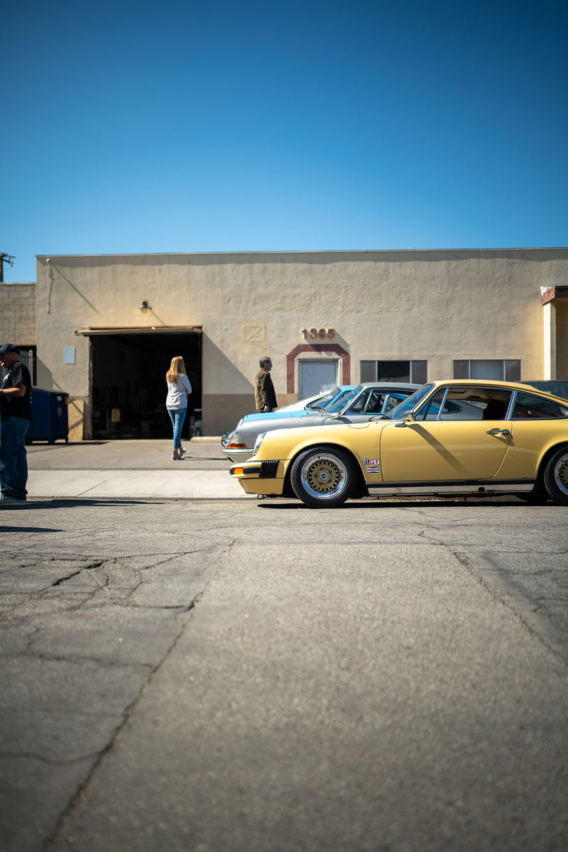 Yellow Porsche 911 with gold mesh rims parked outside a building.