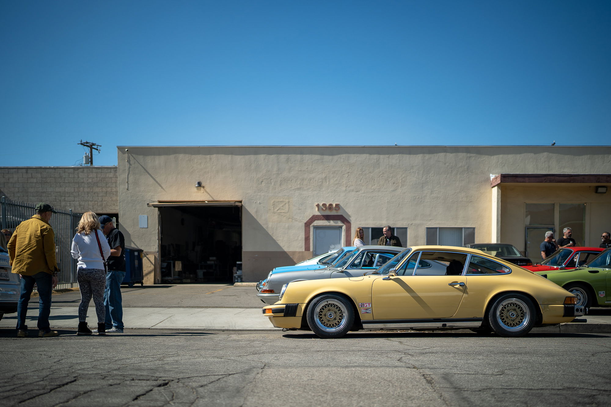 Yellow 1970s Porsche 911 with gold Fuchs rims parked outside a building.