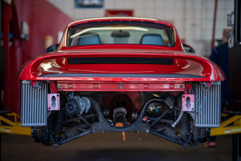 Rear view of a red Porsche 911 undergoing service, with intercoolers visible.