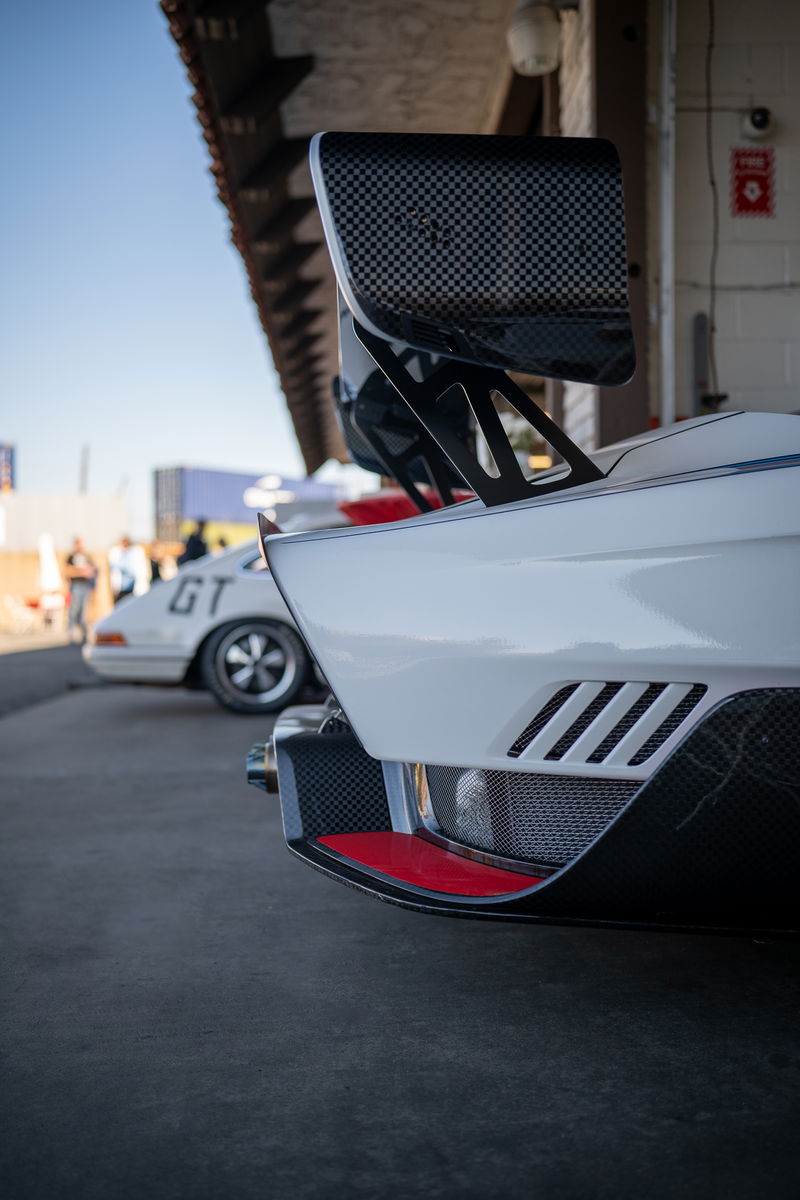 White sports car with carbon fiber wing and red trim.