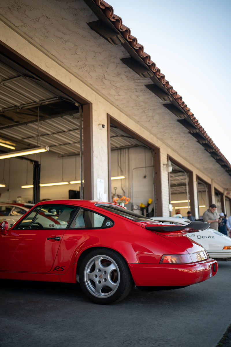 Red Porsche 911 RS with silver Fuchs rims in front of an auto shop.