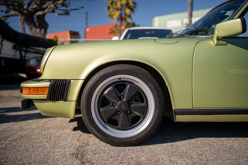 Front fender of a light green Porsche 911 showing its black Fuchs rims.
