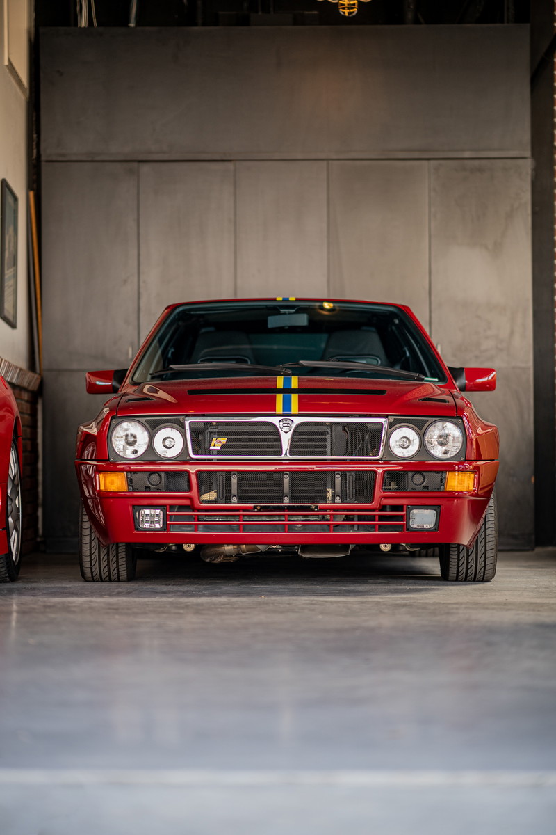 Front view of a red Lancia Delta Integrale with rally livery stripes.