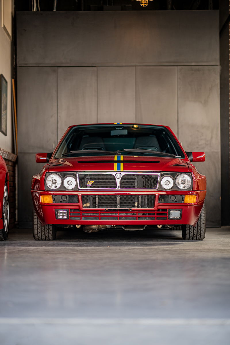 Front view of a red Lancia Delta Integrale with rally livery stripes.