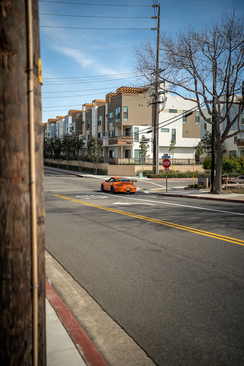 Orange Porsche 911 GT3 touring on street, featuring a prominent rear wing and black trim.