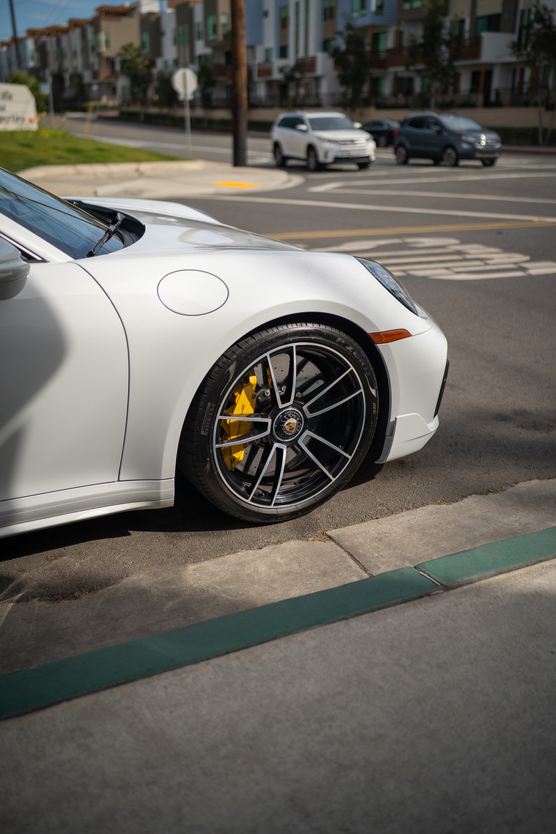 White Porsche 911 Carrera S with black alloy rims and yellow brake calipers.