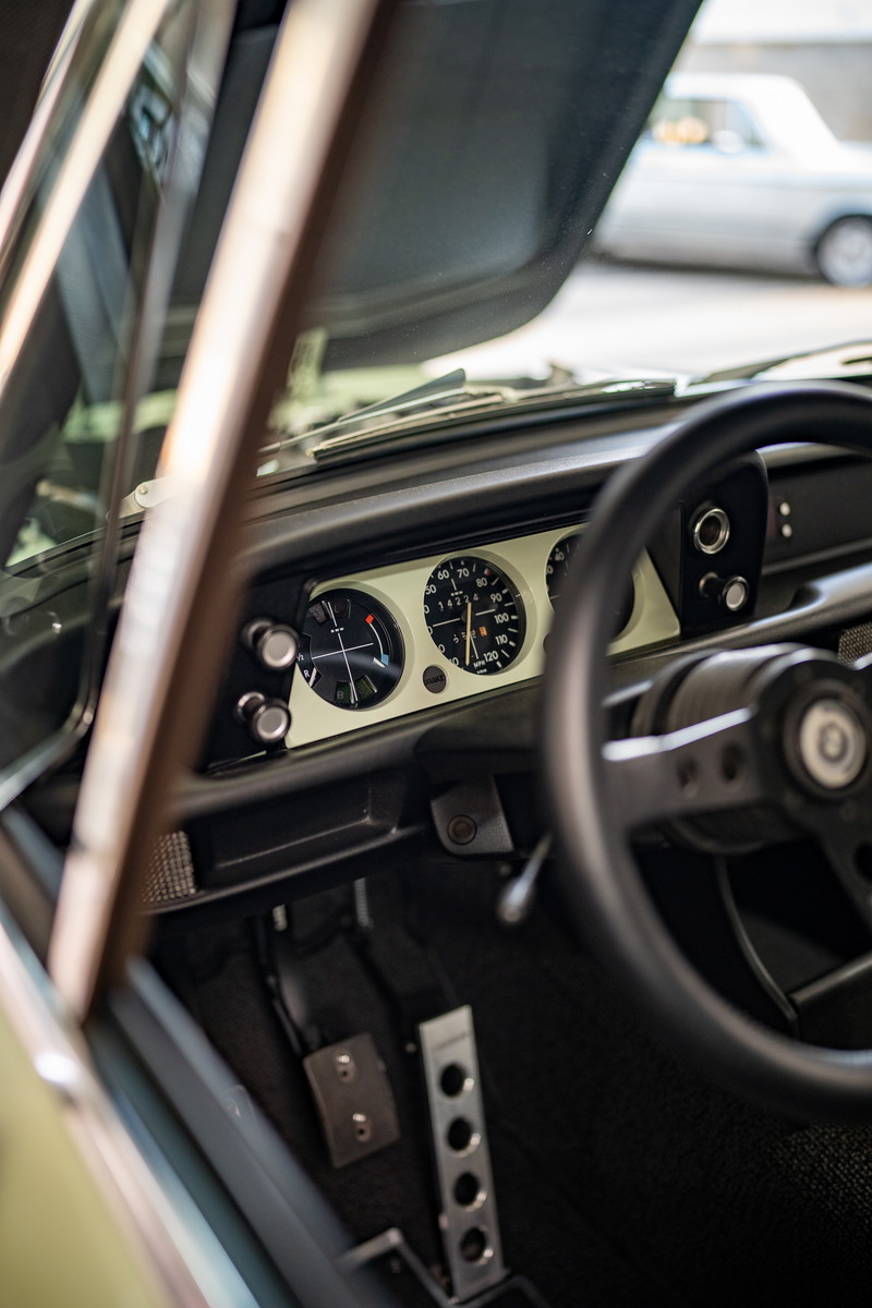 Interior view of a vintage BMW 2002 with classic gauges, sport steering wheel, and floor-mounted pedals.