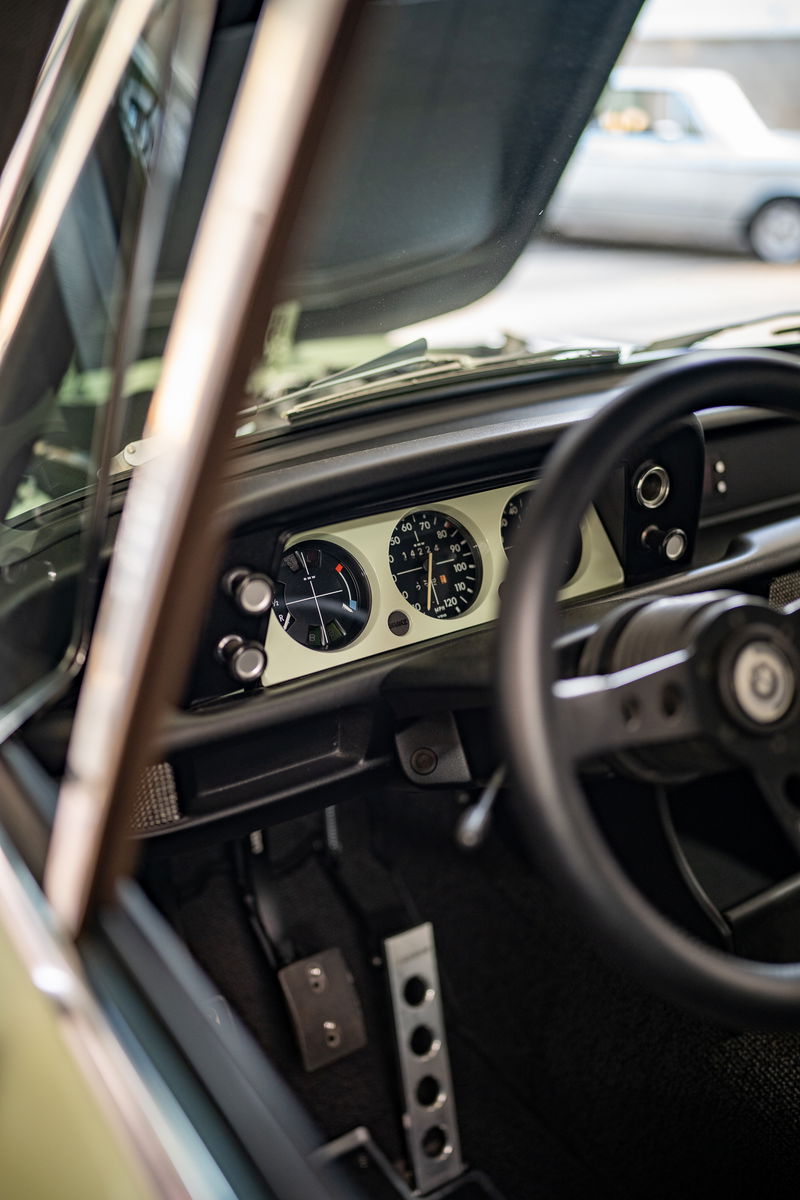 Interior view of a vintage BMW 2002 with classic gauges, sport steering wheel, and floor-mounted pedals.