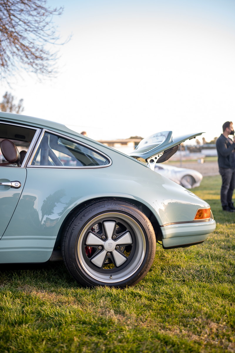 Mint green Porsche 911 with Fuchs rims and ducktail spoiler at a car show.