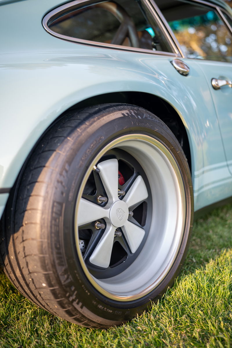 Close up of a light blue classic Porsche 911 with silver Fuchs rims and performance tires.
