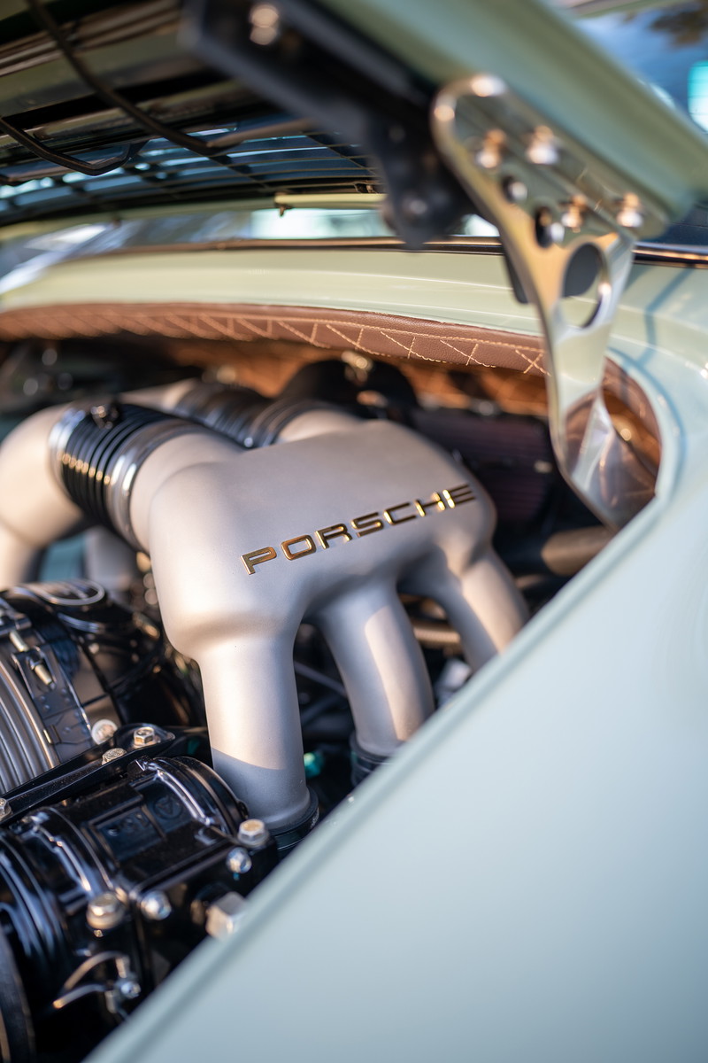 Closeup of a classic Porsche engine with gold "PORSCHE" lettering. Light blue exterior trim.