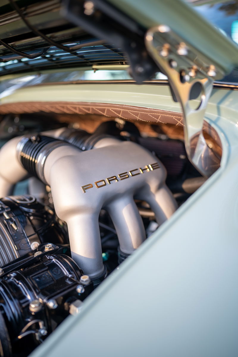 Closeup of a classic Porsche engine with gold "PORSCHE" lettering. Light blue exterior trim.