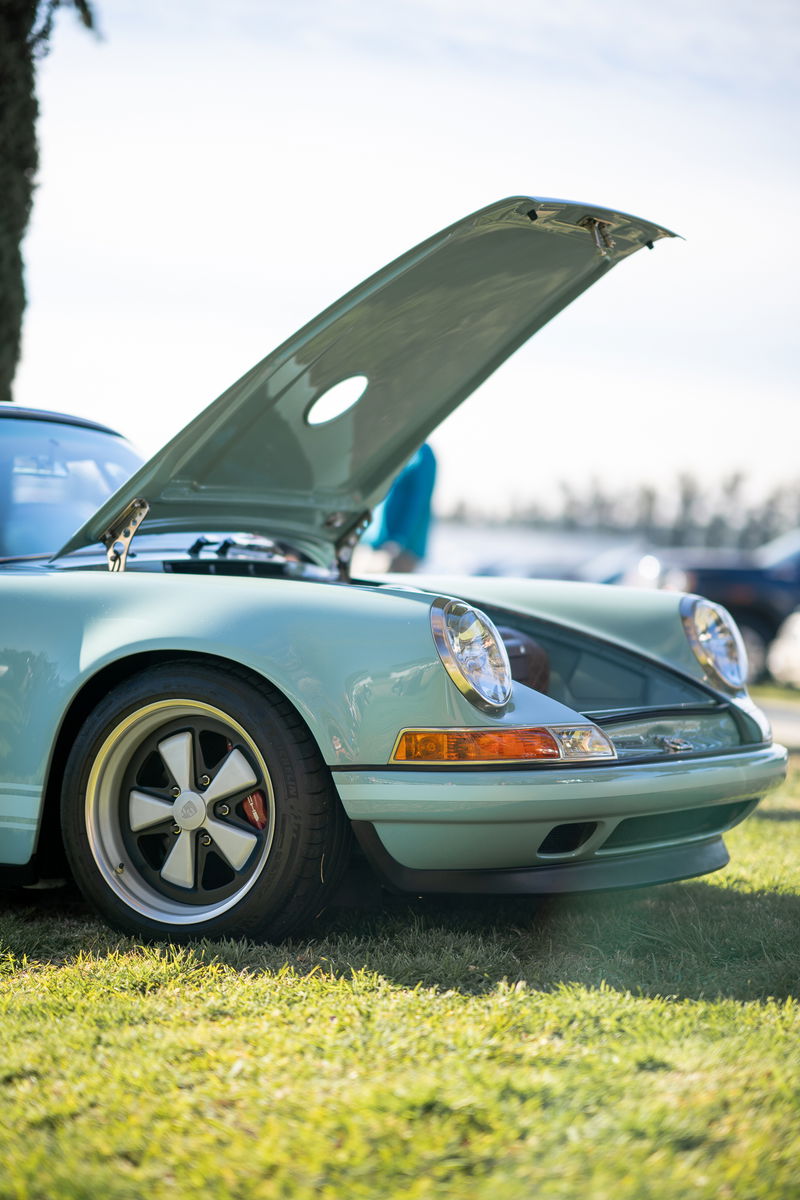 Light blue Porsche 911 with hood open, detailed classic rims, parked on grass.
