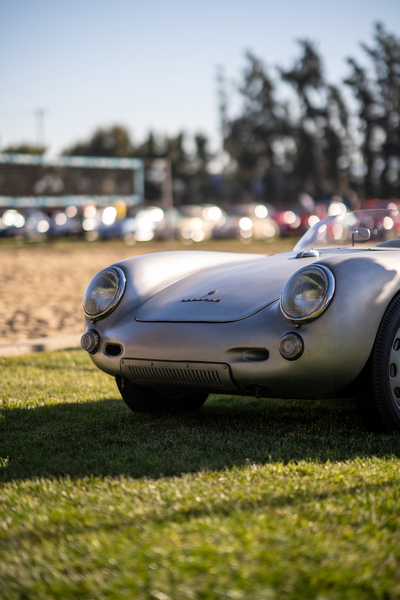 Silver Porsche 550 Spyder front view on grass, parked at a car show with blurred background.