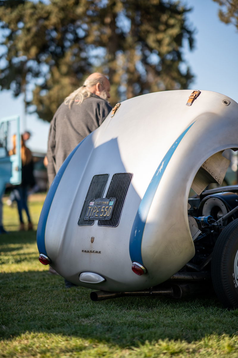 Rear view of a silver Porsche 550 Spyder with blue racing stripes and "TYPE 550" California license plate.