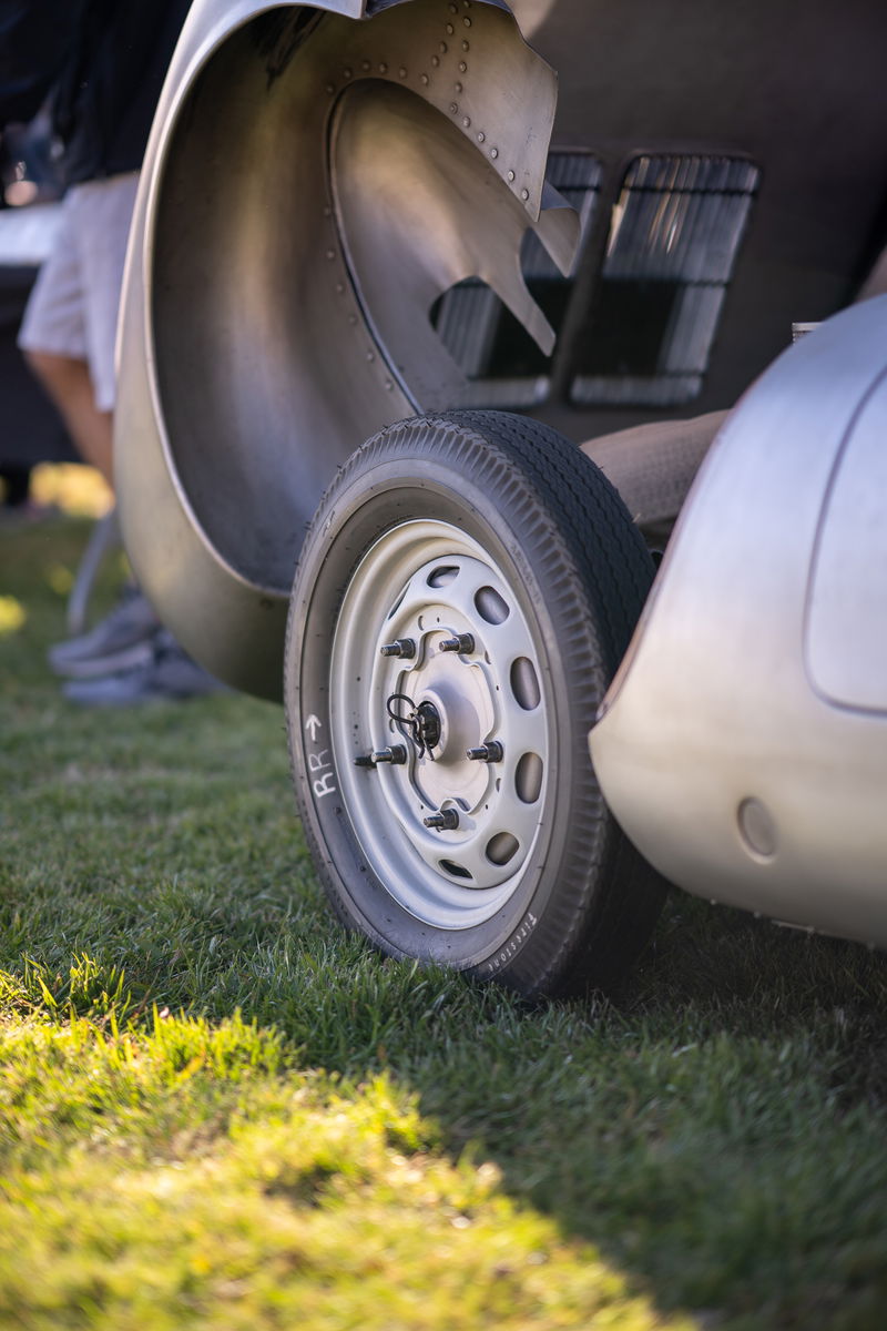 Close-up of a classic silver Jaguar E-Type's rear wheel and riveted aluminum body panel.