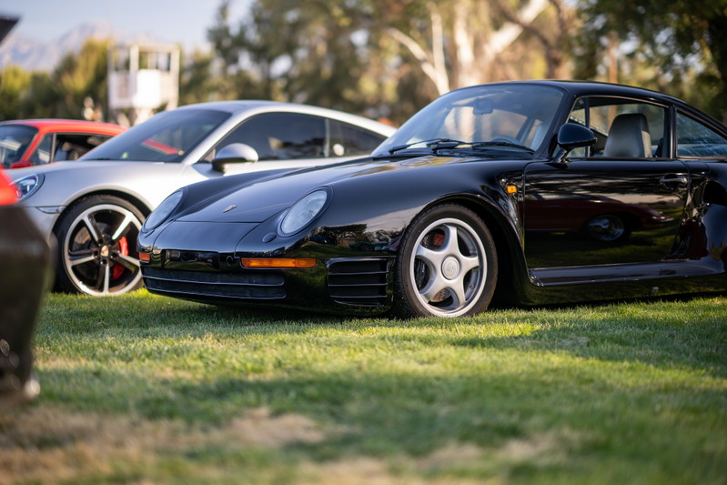 Black Porsche 959 sports car with classic five-star rims parked on grass.