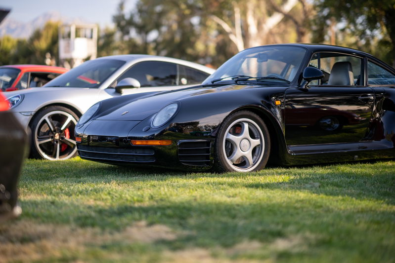 Black Porsche 959 sports car with classic five-star rims parked on grass.