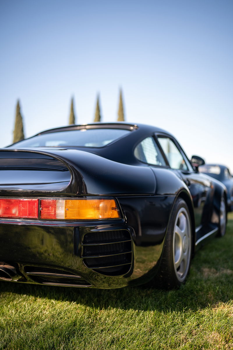 Black Porsche 959 rear quarter panel, showing taillights, vented bumper, and alloy rims.