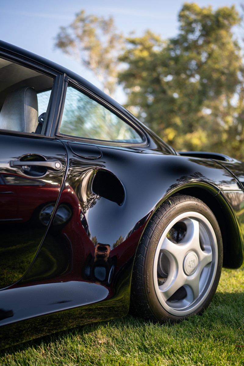 Black Porsche 959 with five-spoke alloy rims, parked on grass.