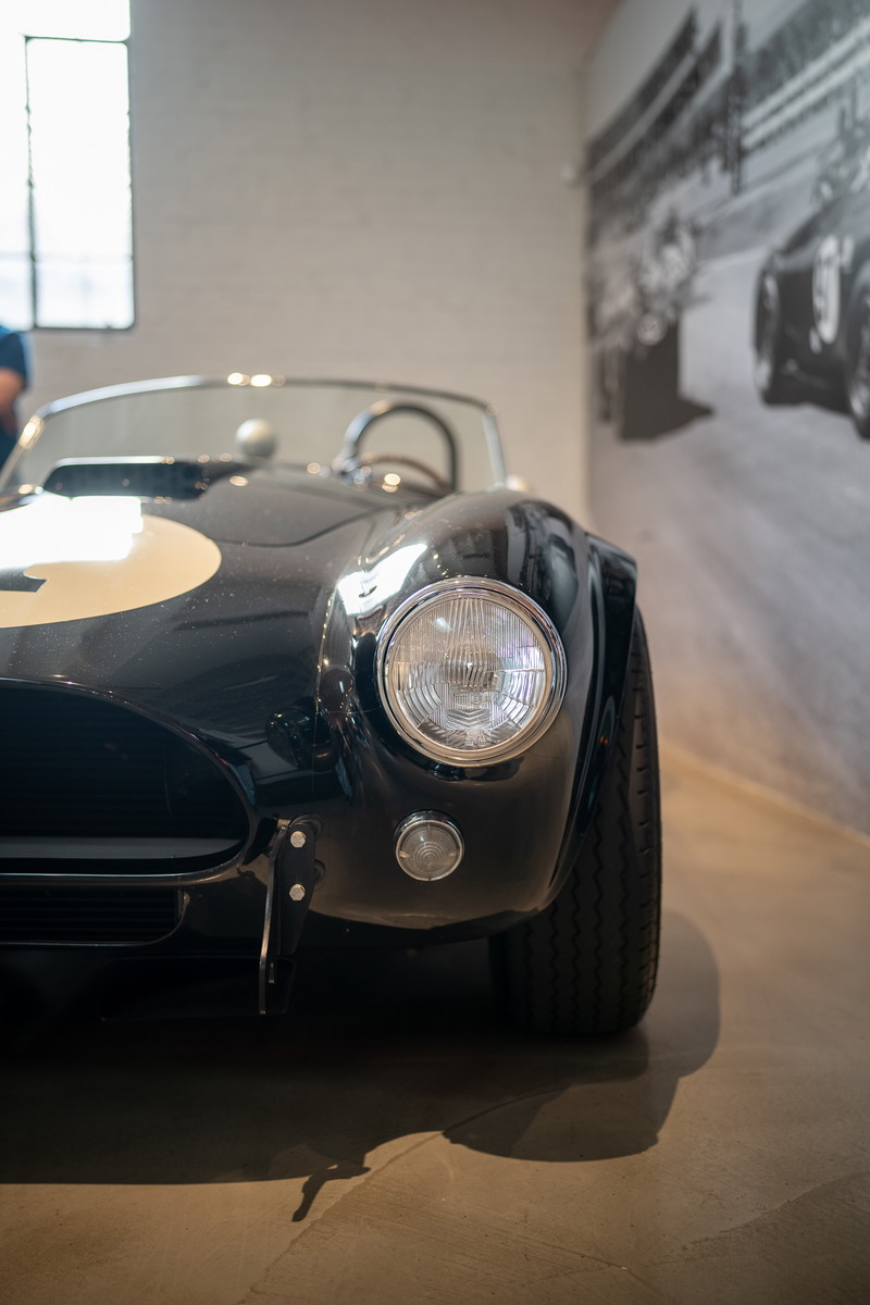 Classic black Shelby Cobra roadster with white racing stripe and #2 on hood. Chrome rims, round headlights.