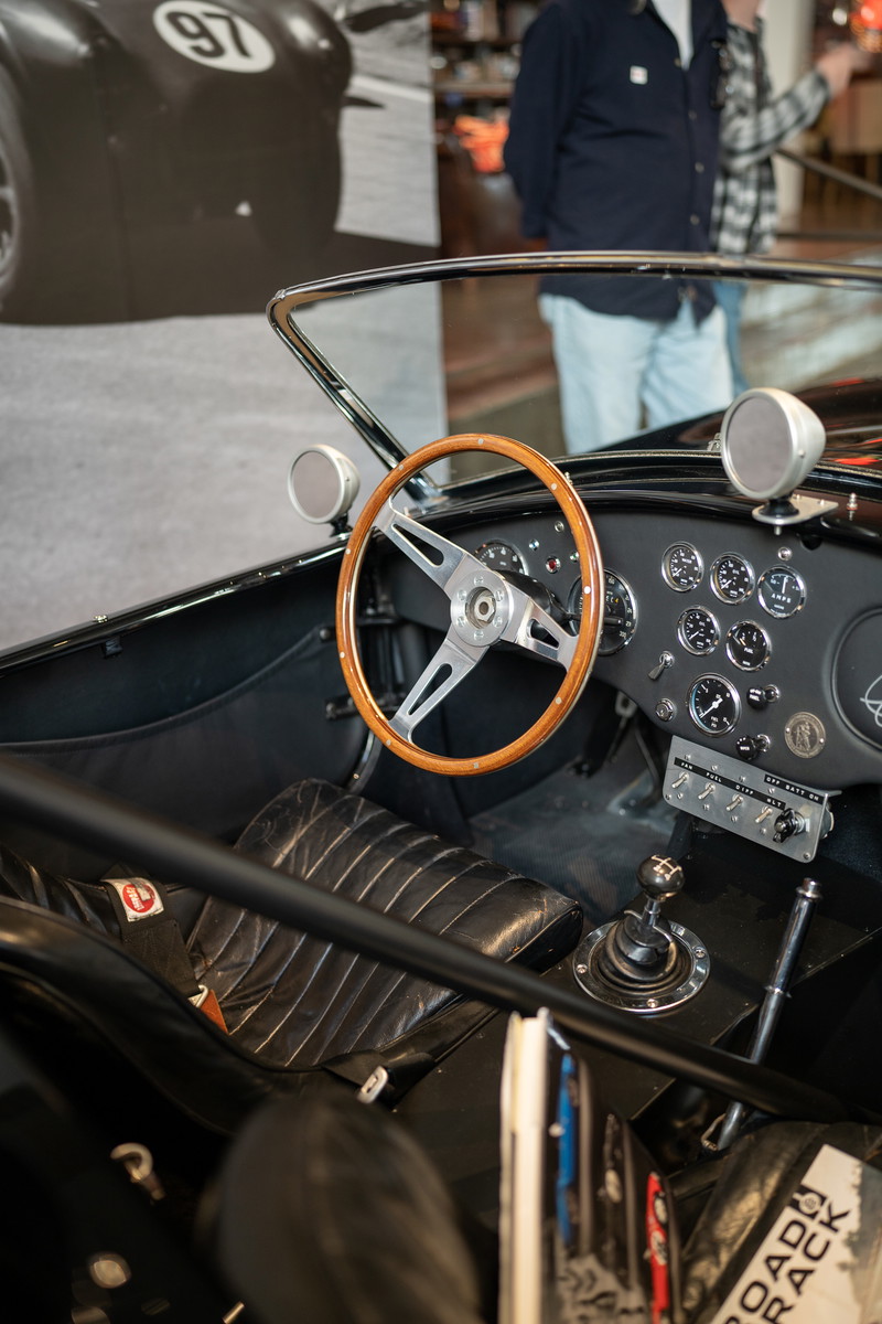 Black Shelby Cobra 427 interior with wooden steering wheel, quilted leather seats, and racing gauges.