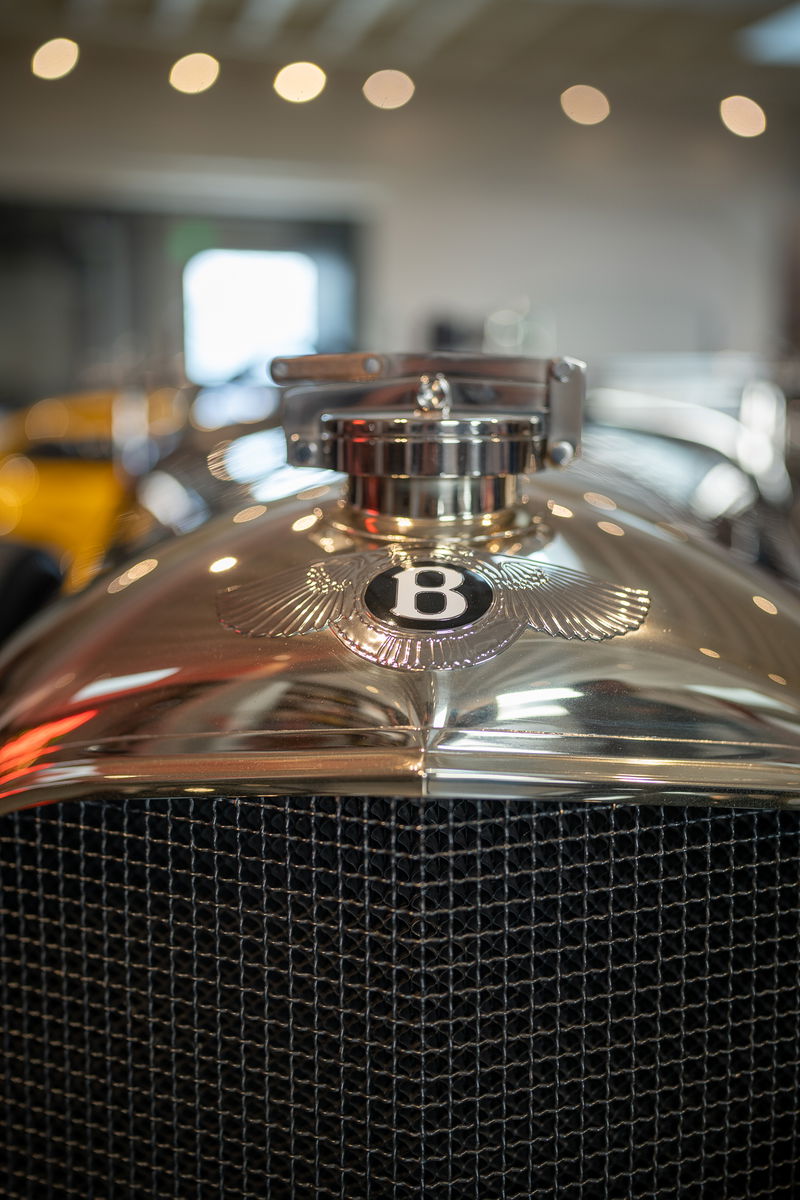 Close-up of a vintage Bentley's polished chrome grille and winged "B" emblem.