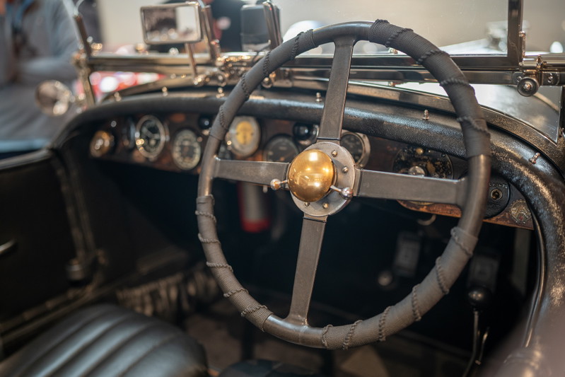 Vintage car dashboard with a metal steering wheel with a brass horn button.