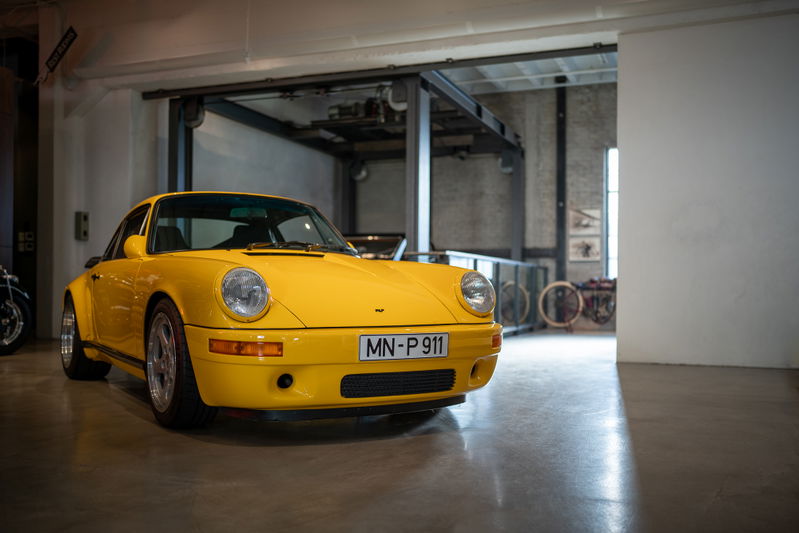 Yellow Porsche 911 with silver rims and black trim, shown in a garage with a lift.
