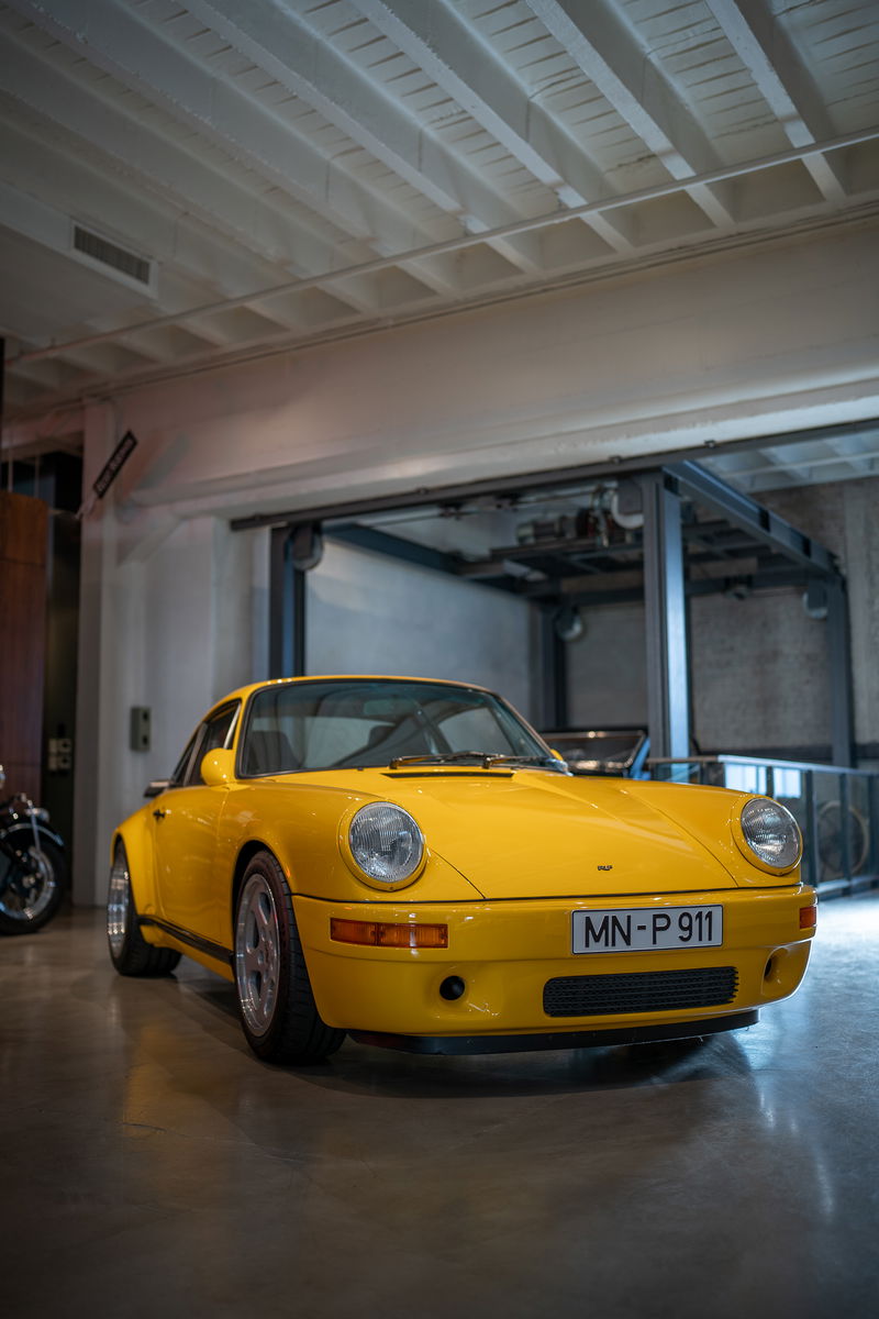 Yellow Porsche 911 with silver rims and black trim in a garage.