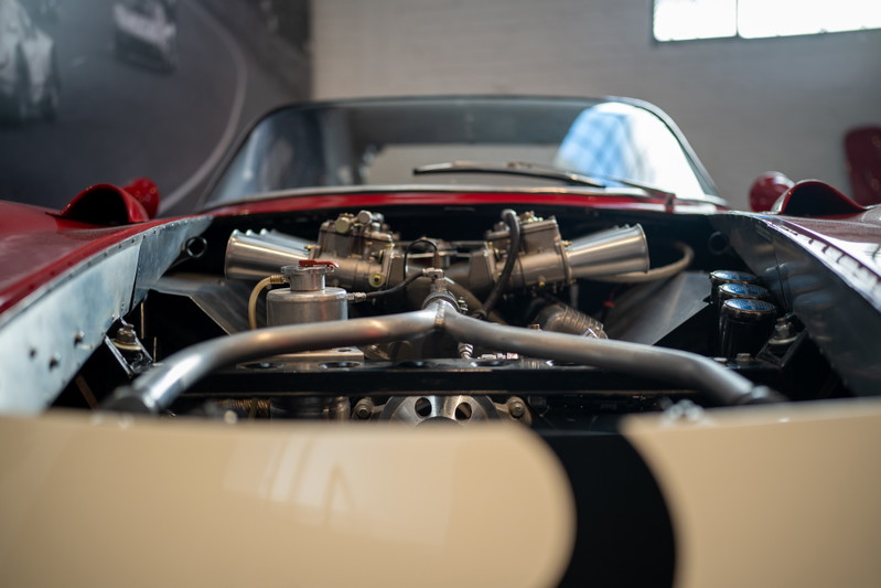 Vintage race car engine with dual carburetors and polished metal intake piping.