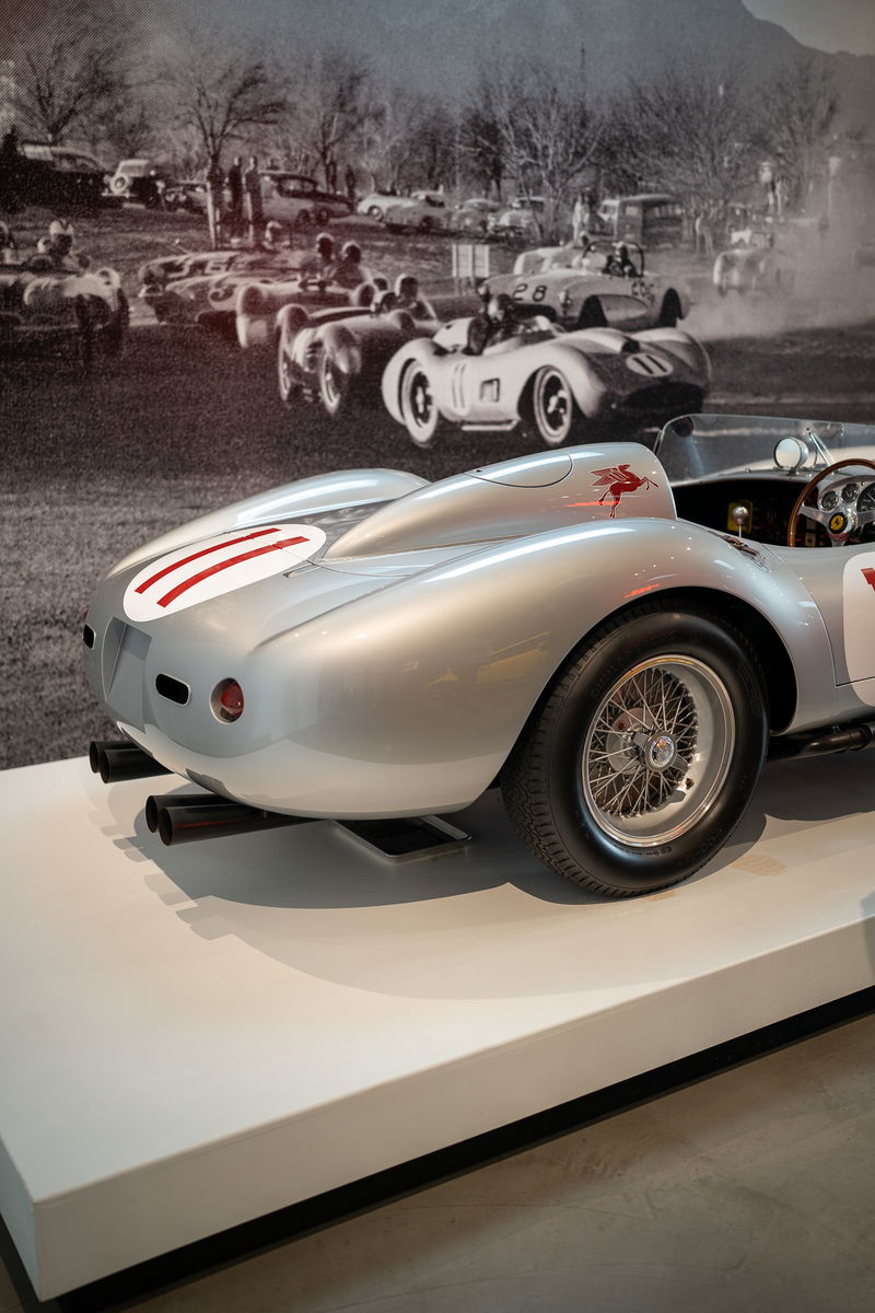 Silver 1950s race car with red stripe livery, wire rims, and Pegasus emblem.