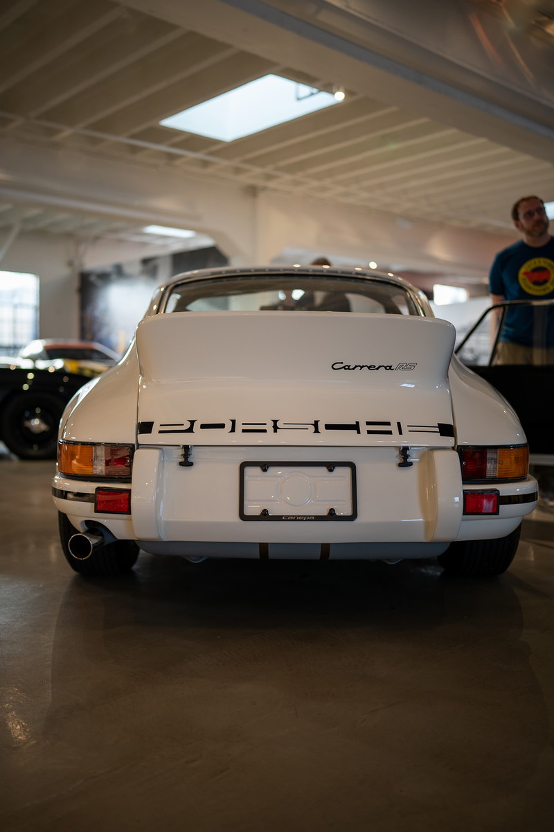 Rear view of a white 1973 Porsche 911 Carrera RS with black trim and a chrome exhaust pipe.