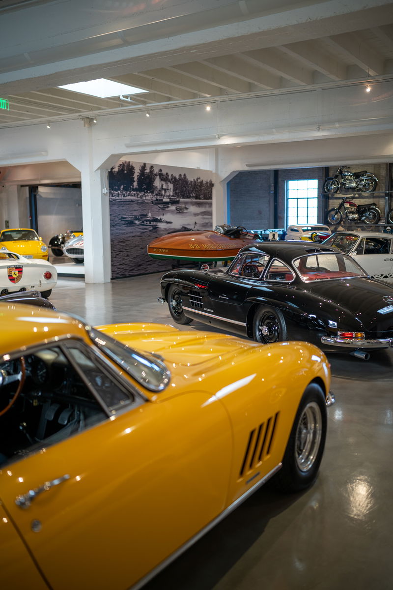 Yellow Ferrari 275 GTB with chrome trim and wire-spoke rims in a showroom.