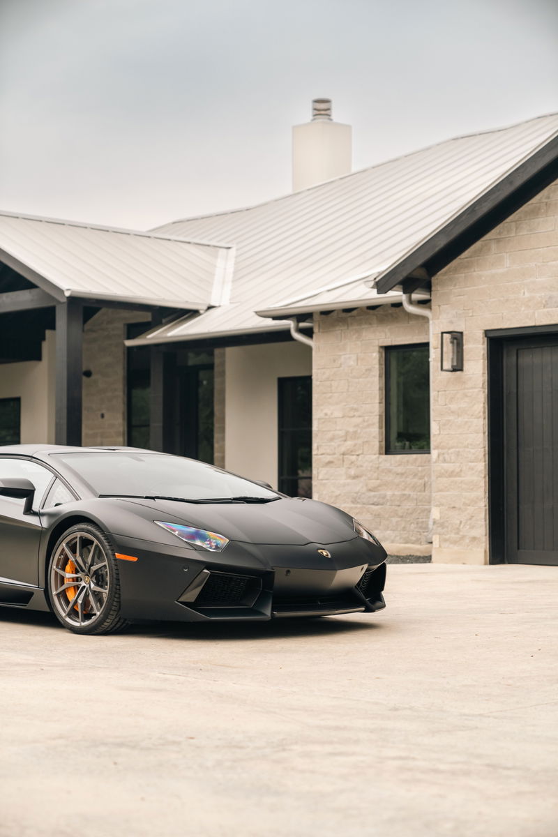 Matte black Lamborghini Aventador LP700-4 with orange brake calipers and silver multi-spoke rims.