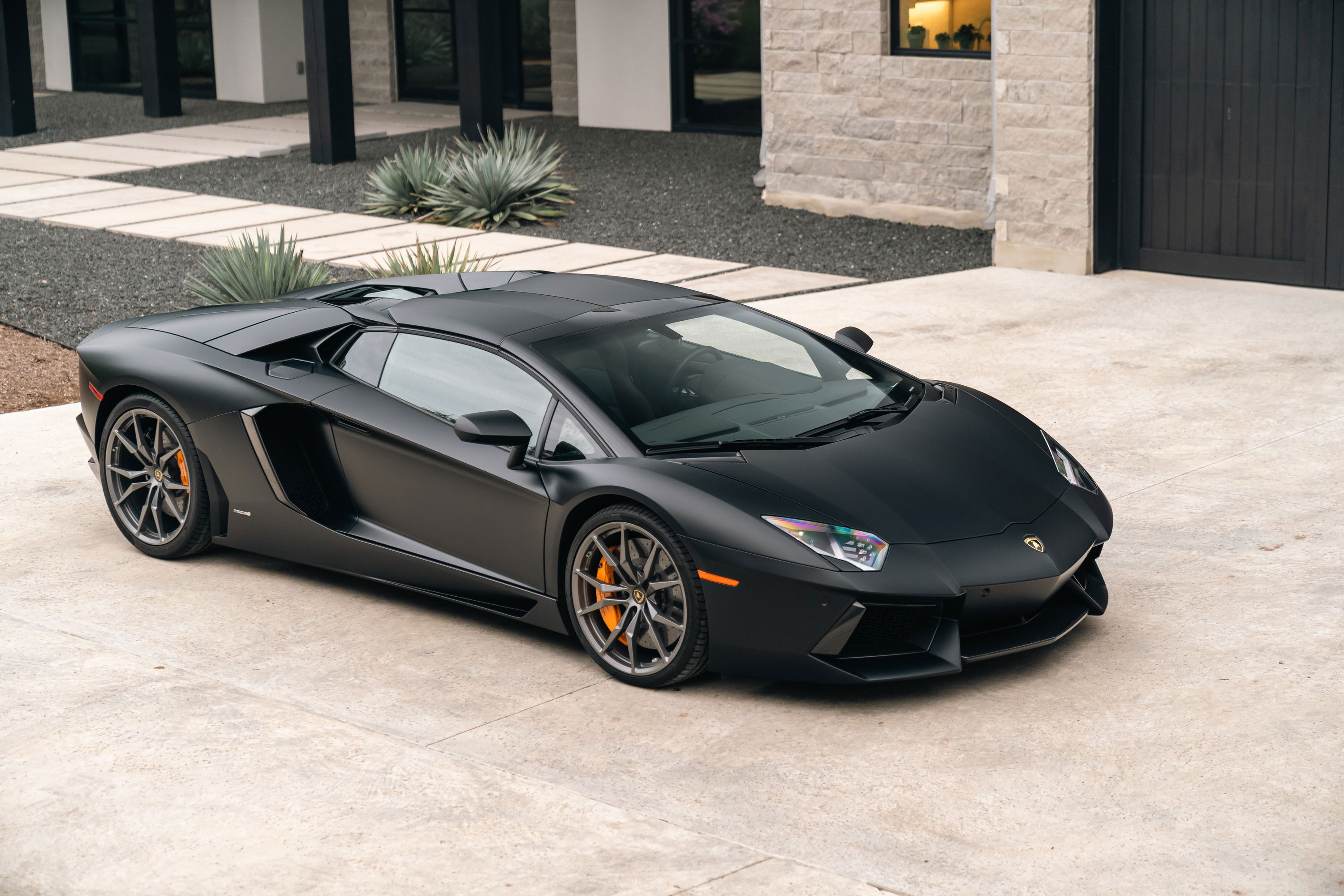 Matte black 2014 Lamborghini Aventador LP700-4 with orange brake calipers and dark grey rims.