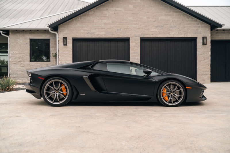 Matte black Lamborghini Aventador LP700-4 with gray rims and orange brake calipers.