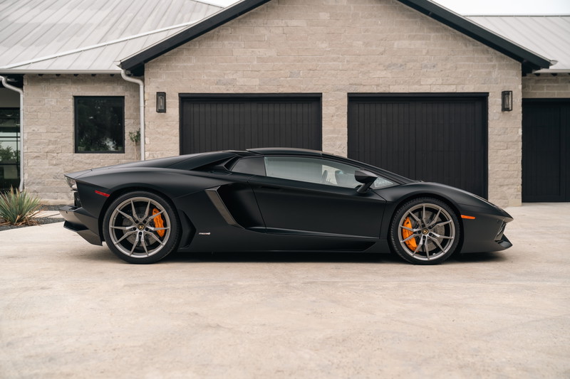Matte black Lamborghini Aventador LP700-4 with gray rims and orange brake calipers.