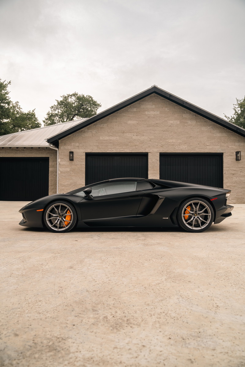 Matte black Lamborghini Aventador LP700-4 with silver rims and orange brake calipers.