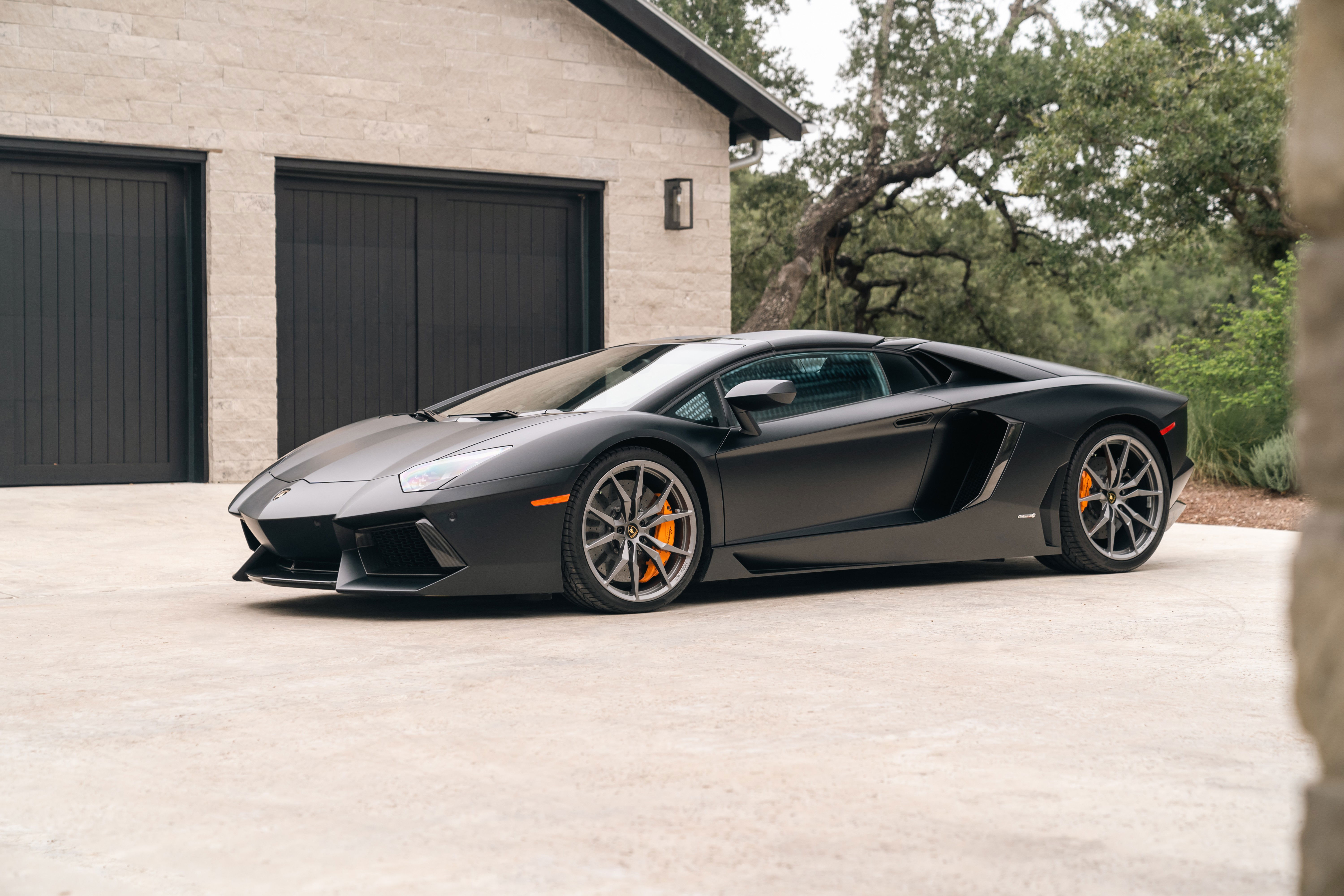 Matte black Lamborghini Aventador LP700-4 with orange brake calipers and grey rims.