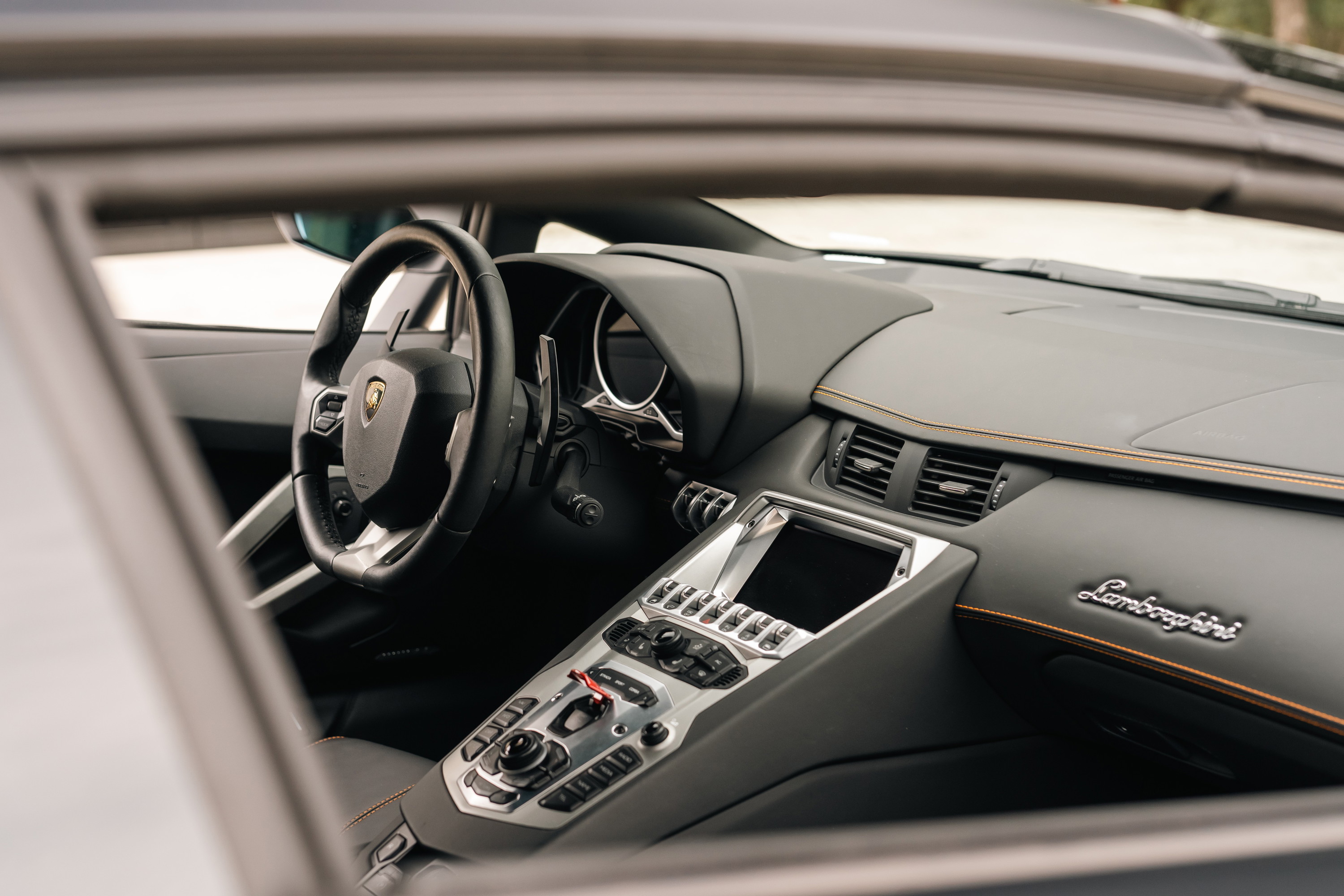 Interior of a black Lamborghini Aventador LP700-4 with orange trim and silver accents.