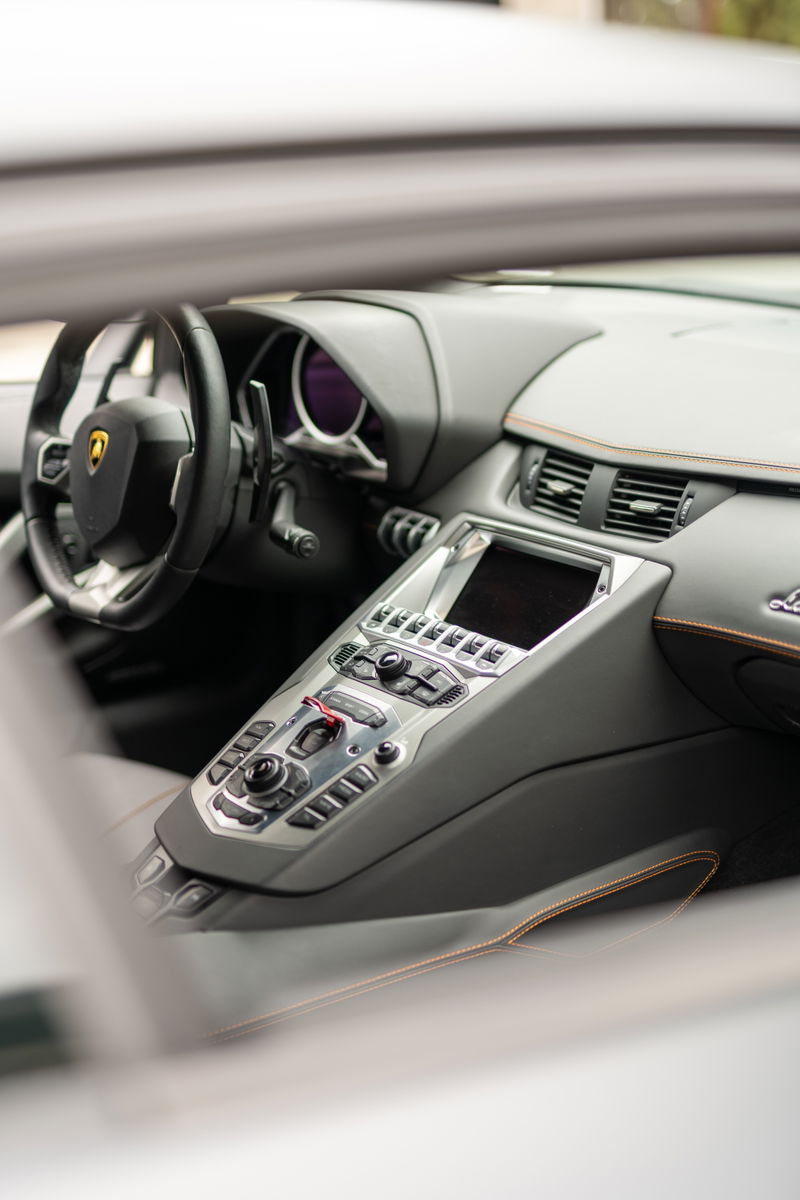 Lamborghini Aventador LP700-4 interior featuring carbon fiber trim, leather seats with orange stitching, and a central console.