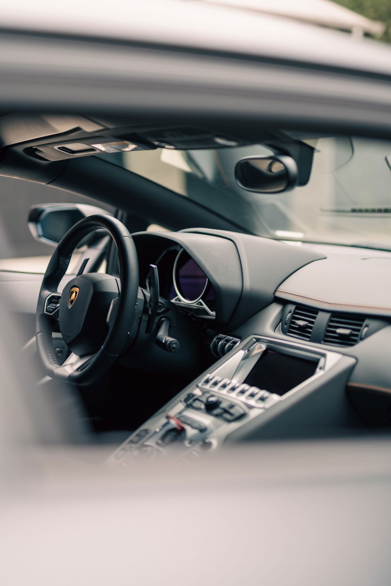 Interior view of a Lamborghini Aventador LP700-4 dashboard, featuring a leather-wrapped steering wheel and center console.